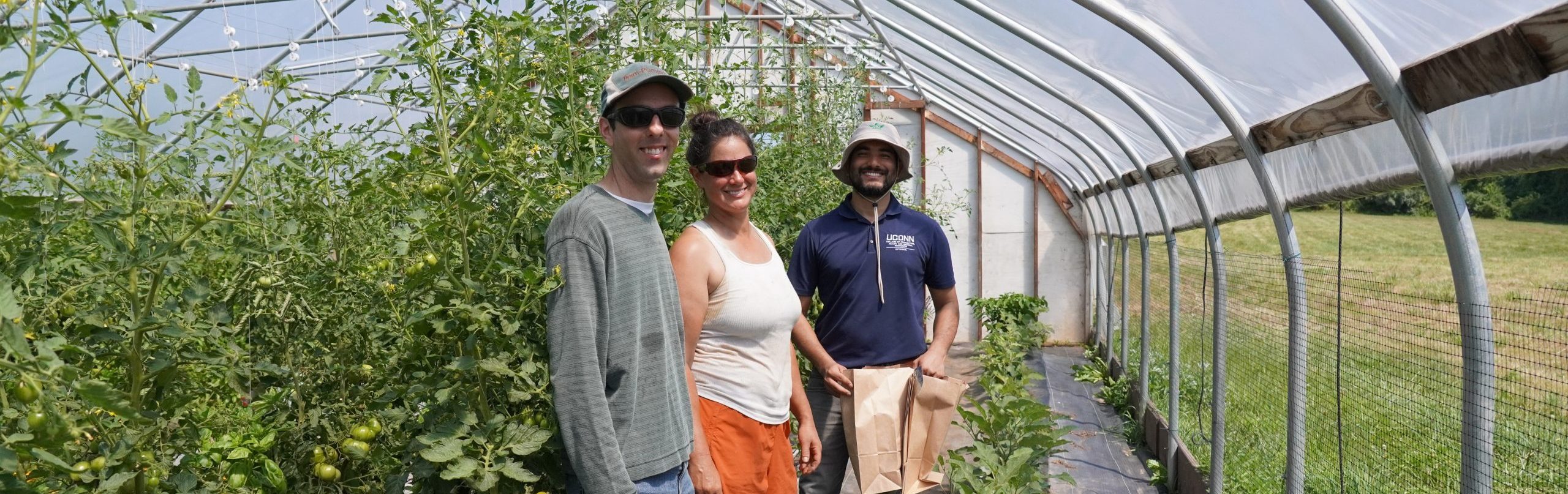 3 people smiling at the camera as they stand in a high tunnel